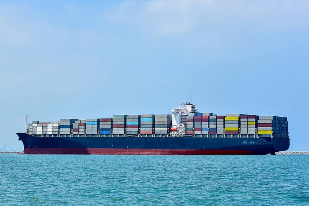 A huge container cargo ship sailing in the open sea under a cloudy sky.